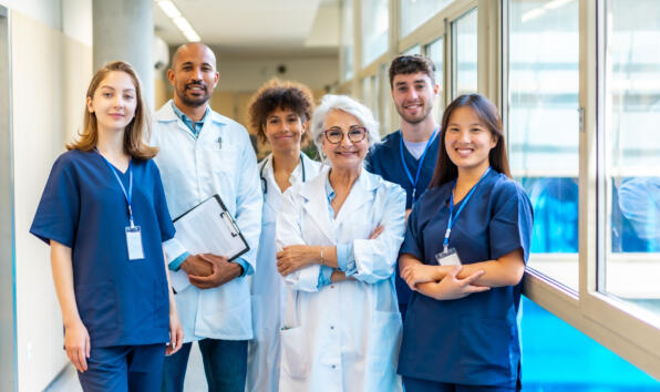 Portrait featuring a multi-ethnic medical team smiling confidently at the camera while gathered in a bustling hospital corridor