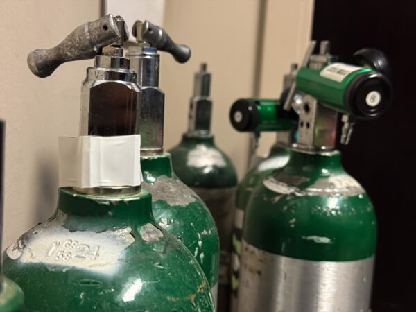 Worn oxygen tanks stored in a healthcare facility, showing close-up texture and valves. Essential for emergency respiratory support in clinical settings.